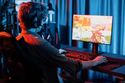 Host channel of young gaming streamer, team gamer playing battle game shooting with multiplayer at warship on pc screen with back side image, wearing headset with mic at digital neon room. Gusher.