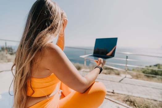 Digital nomad, Business woman working on laptop by the sea. Pretty lady typing on computer by the sea at sunset, makes a business transaction online from a distance. Freelance, remote work on vacation