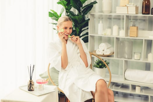 Woman holding slices of fresh cucumber and wearing bathrobe enjoying luxurious facial skincare spa in resort or hotel. Skin treatment for face and beauty care. Quiescent