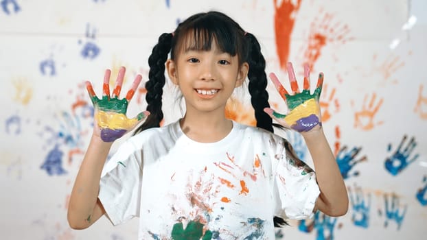 Asian happy student put hands up together show colorful stained hands. Smiling girl standing in front white background with stained hands while looking at camera. Creative activity concept. Erudition.