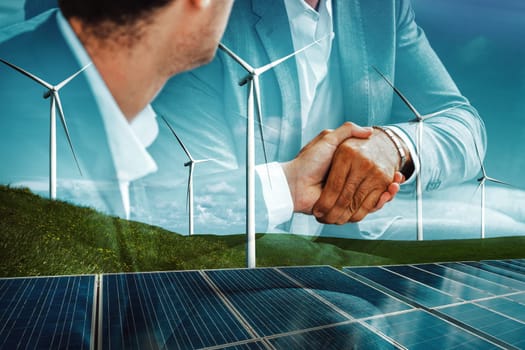 Double exposure graphic of business people handshake over wind turbine farm and green renewable energy worker interface. Concept of sustainability development by alternative energy. uds