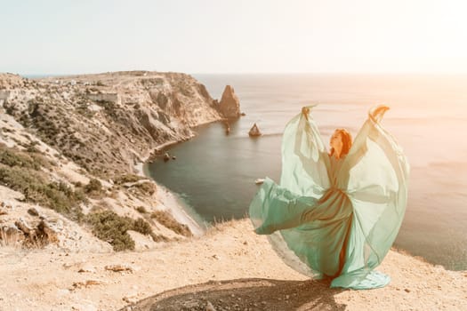 Woman green dress sea. Female dancer posing on a rocky outcrop high above the sea. Girl on the nature on blue sky background. Fashion photo