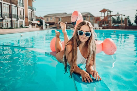 A woman is laying on a pool float in a pool. She is wearing a white bikini and sunglasses