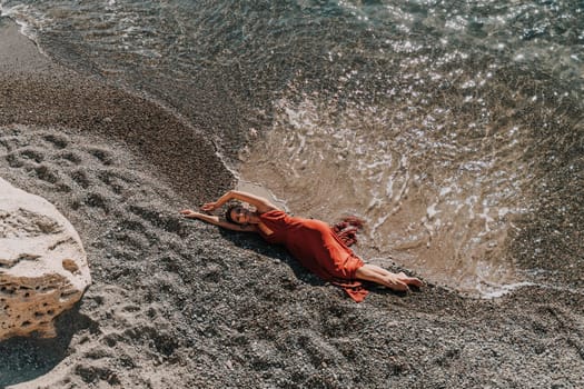 Woman red dress sea. Female dancer in a long red dress posing on a beach with rocks on sunny day.