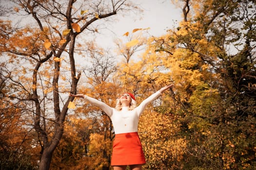 A woman is standing in a field of yellow leaves, wearing a red skirt and a white shirt. She is smiling and she is enjoying the autumn season