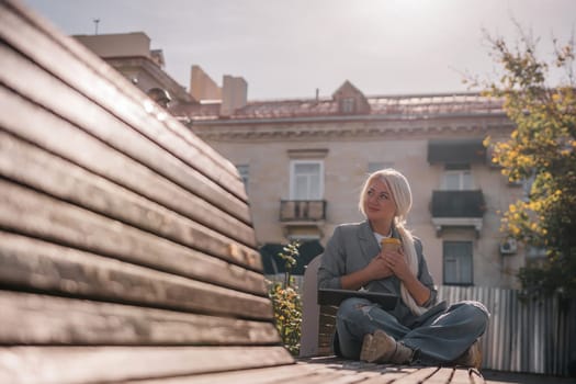 A woman sitting on a bench with a cell phone in her hand. She is wearing a suit and she is working on her phone