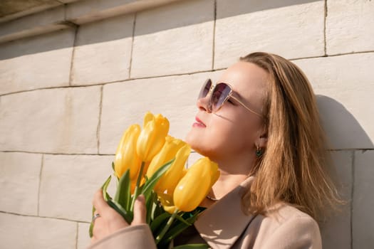 Woman holding yellow tulips, leaning against stone wall. Women's holiday concept, giving flowers