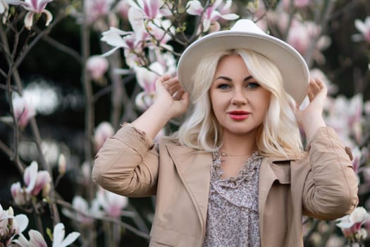 Magnolia flowers woman. A blonde woman wearing a white hat stands in front of a tree with pink flowers. She has a smile on her face and she is enjoying the beautiful scenery