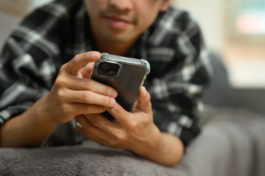 Cropped shot adult asian man lying on couch and using mobile phone.