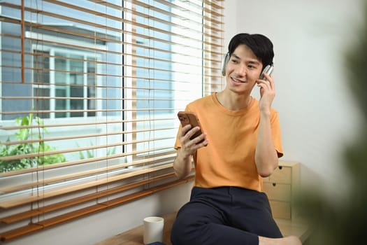 Portrait of positive young asian man listening to music in headphones and looking away.