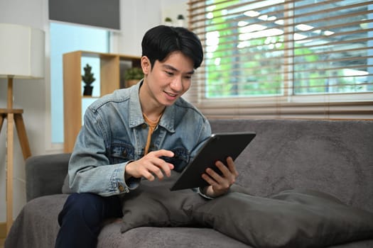 Creative man freelancer using digital tablet on couch at home.