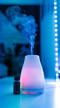 One pink electric air freshener with a bottle of aromatic oil lie on a table in a home beauty salon in neon light with evaporating steam and reflection in the mirror, close-up side view with selective focus.