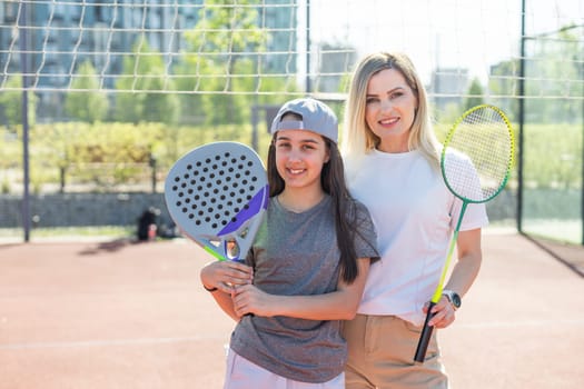 Happy caucasian mother and daughter playing padel tennis and badminton on tennis court outdoors. High quality photo
