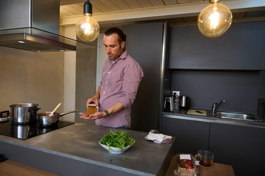 Male chef cook preparing Italian pasta at home. Young Caucasian man standing at electric stove, putting raw whole grain spaghetti capellini into a stainless steel saucepan with boiling water.