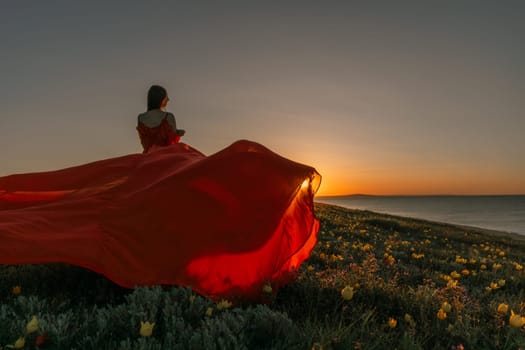 A woman in a red dress is standing in a field with the sun setting behind her. She is reaching up with her arms outstretched, as if she is trying to catch the sun. The scene is serene and peaceful