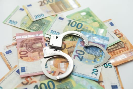 Pair of metal police handcuffs on Euros banknotes money cash background. Corruption, dirty money, gambling or financial crime ideas concept. High quality photo