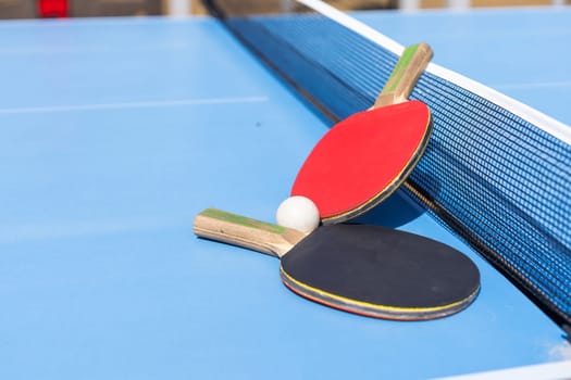 Two table tennis or ping pong rackets and ball on blue table with net. High quality photo