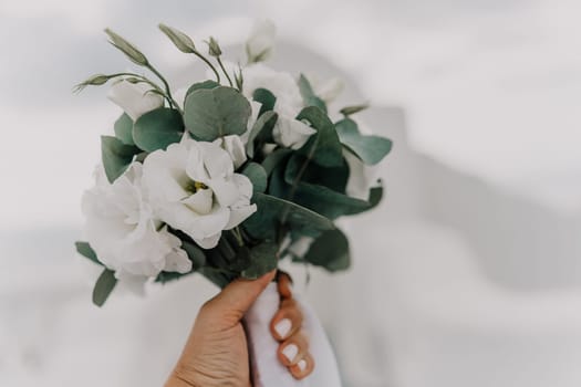 A bouquet of white flowers with green leaves is being held by a person's hand. The arrangement is simple and elegant, with the white flowers providing a clean and fresh look