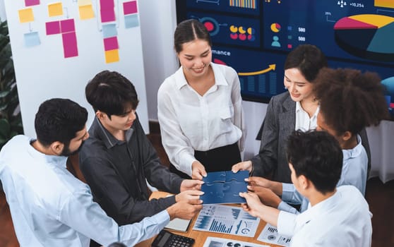 Corporate officer worker collaborate in office, connecting puzzle pieces with report paper on table as partnership and teamwork. Unity and synergy in business concept by merging jigsaw puzzle. Concord