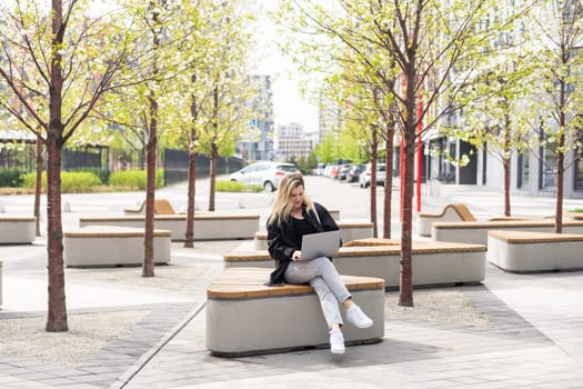 Young beautiful business woman sitting on a bench in the sunny city. High quality photo