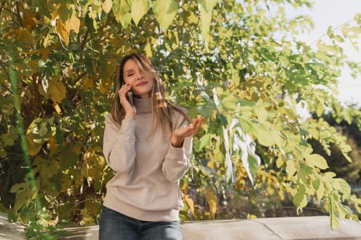 A woman is talking on her cell phone while sitting under a tree. She is smiling and she is enjoying her conversation