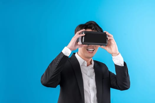Smiling Asian businessman looking thorough VR connecting to business world report in futuristic metaverse, analyzing innovation technology ads in virtual reality isolated blue copyspace. Contrivance.