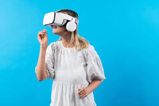 Girl smells flower while wearing VR glasses at blue background. Happy woman with VR goggle enjoy looking nature hologram while connection with visual reality world. Technology innovation. Contraption.