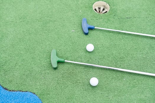 Mini-golf clubs and balls of different colors laid on artificial grass. High quality photo