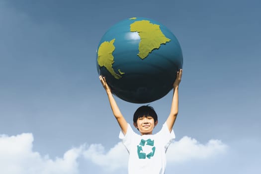 Young asian boy holding big planet Earth globe at sky and cloudscape background as Earth day to save this planet with ESG principle and environment friendly energy for brighter future. Gyre