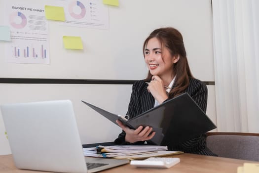 Cheerful business lady working on laptop in office, Asian happy beautiful businesswoman in formal suit work in workplace. Attractive female employee office worker smile..