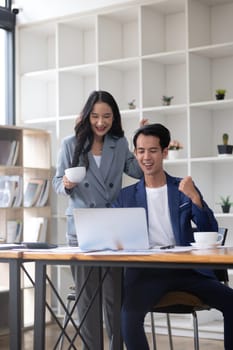 A young businessman and a successful Asian accountant happily celebrate together in the office..