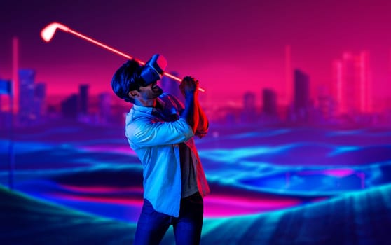 Caucasian man playing golf in metaverse while wearing VR goggles to enter simulated virtual world. Handsome gamer using virtual reality glasses enter in neon golf course. Innovation. Sport. Deviation.