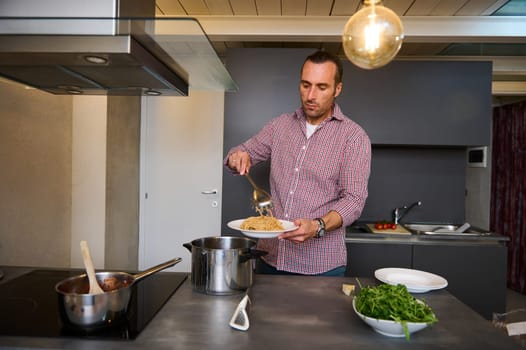 Authentic portrait of a handsome guy at home kitchen, plating up freshly cooked spaghetti, preparing healthy dinner for family, according to traditional Italian. People. Food and drink consumerism