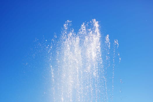 A liquid fountain spraying water against an electric blue sky, creating a stunning natural landscape with trees and clouds in the background