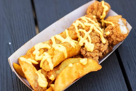A fast food staple, the cardboard container holds a delicious combination of french fries and chicken. This fried food dish is a popular choice for those craving a satisfying and savory meal