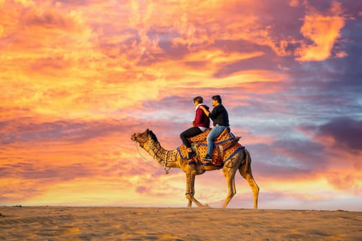 Jaisalmer, Rajasthan, India - 25th Dec 2023: Young couple tourists sitting on camel enjoying the walk sand dunes in sam or dubai