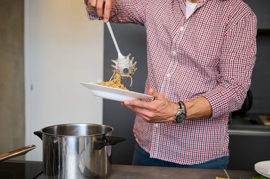 Close-up male chef pouring freshly cooked Italian past into a white plate, ready to serve it to the customers. Food and drink consumerism. Culinary. Epicure. Man cooking Italian spaghetti for dinner