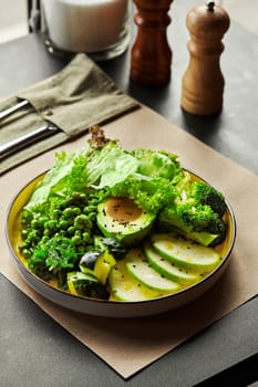 Stylish table setting with plate of green salad with fresh avocado, zucchini, cucumber, peas, broccoli, lettuce, and wakame hiyashi seasoned with peanut dressing and garnished with black sesame