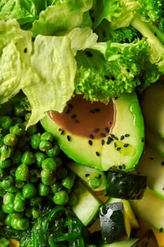 Macro view of fresh green vegetarian salad of avocado, peas, lettuce, cucumber and wakame hiyashi dressed with peanut sauce and sprinkled with black sesame. Natural colorful food background