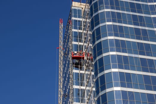 A towering skyscraper against a clear blue sky, showcasing modern urban design with a mix of condominiums and commercial buildings, with a construction crane in the background