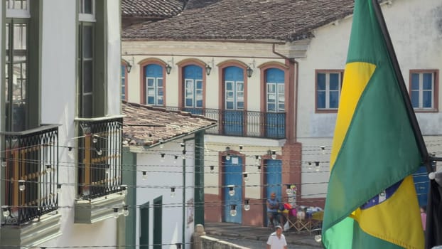"Brazilian flag waves in front of a bustling street with people passing by."