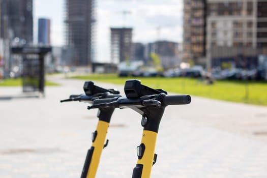 A black and yellow scooter with an electric blue bicycle handlebar is parked on the side of the asphalt road in the city, blending in with the metal car passing by. A vehicle for recreation