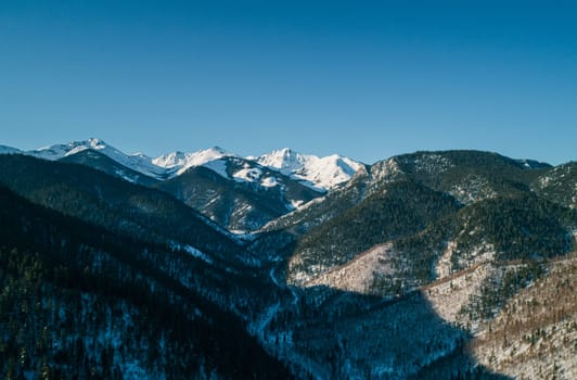 Aerial landscape mountains covered with forest and snow-capped peaks in the background. Cinematic winter mountains landscape