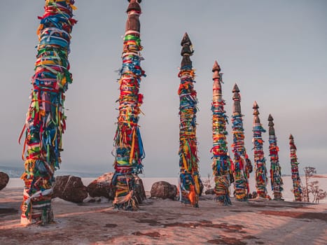 Traditional buryat shaman sacred pillars with colorful ribbons in winter at sunset, cape Burkhan, Olkhon island. Winter Baikal.