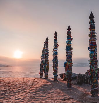 Traditional buryat shaman sacred pillars with colorful ribbons in winter at sunset, cape Burkhan, Olkhon island. Winter Baikal.