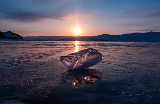 Ice crystal on the frozen surface of Lake Baikal in early morning. Sky and sun reflections on the ice surface. Amazing winter landscape. Winter tourist season at lake Baikal