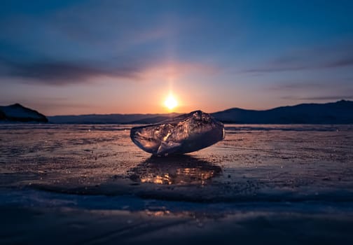Ice crystal on the frozen surface of Lake Baikal in early morning. Sky and sun reflections on the ice surface. Amazing winter landscape. Winter tourist season at lake Baikal