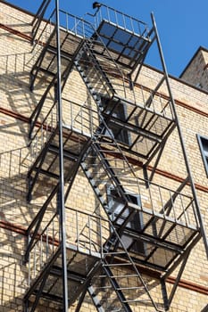 A fire escape made of wood is attached to the buildings facade in the city. It provides an escape route from the condominium through a window to the roof, avoiding overhead power lines