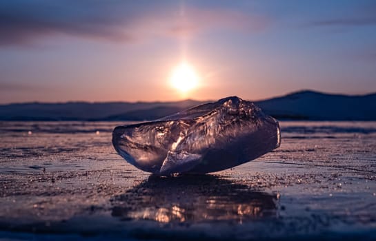 Ice crystal on the frozen surface of Lake Baikal in early morning. Sky and sun reflections on the ice surface. Amazing winter landscape. Winter tourist season at lake Baikal