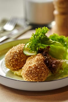 Two deep-fried golden crispy-breaded chicken patties nestled on bed of smooth mashed potatoes garnished with fresh lettuce leaves served on plate. Ideal choice for hearty and traditional meal